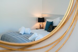 Ein ordentlich bezogenes Bett mit aufgerollten Handtüchern, einer Nachttischlampe und einem blumigem Kopfkissen.