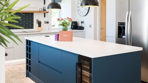 A modern kitchen with a white countertop, blue cabinetry, a built-in wine cooler, and a stainless steel refrigerator.
