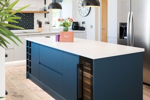A modern kitchen with a white countertop, blue cabinetry, a built-in wine cooler, and a stainless steel refrigerator.