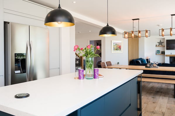 A modern kitchen with a central island, pendant lights, and a dining area with a wooden table and chairs.