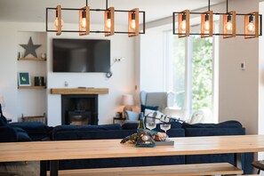 A modern living room with a wooden dining table, blue sofas, and a TV mounted on the wall.