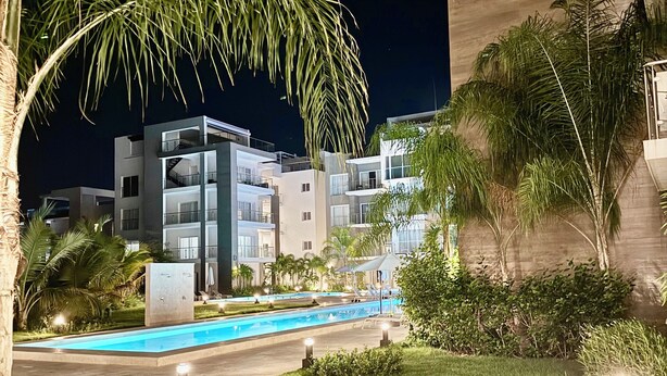 A modern hotel with a swimming pool, surrounded by well-maintained lawns and palm trees. - Gorgeous,  Resort Style Apartment Across Hard Rock Hotel & Casino, Punta Cana (Punta Cana)