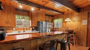 A wooden cabin interior with a kitchen area, bar stools, and a refrigerator. - Encino Pines (Big Bear Lake)