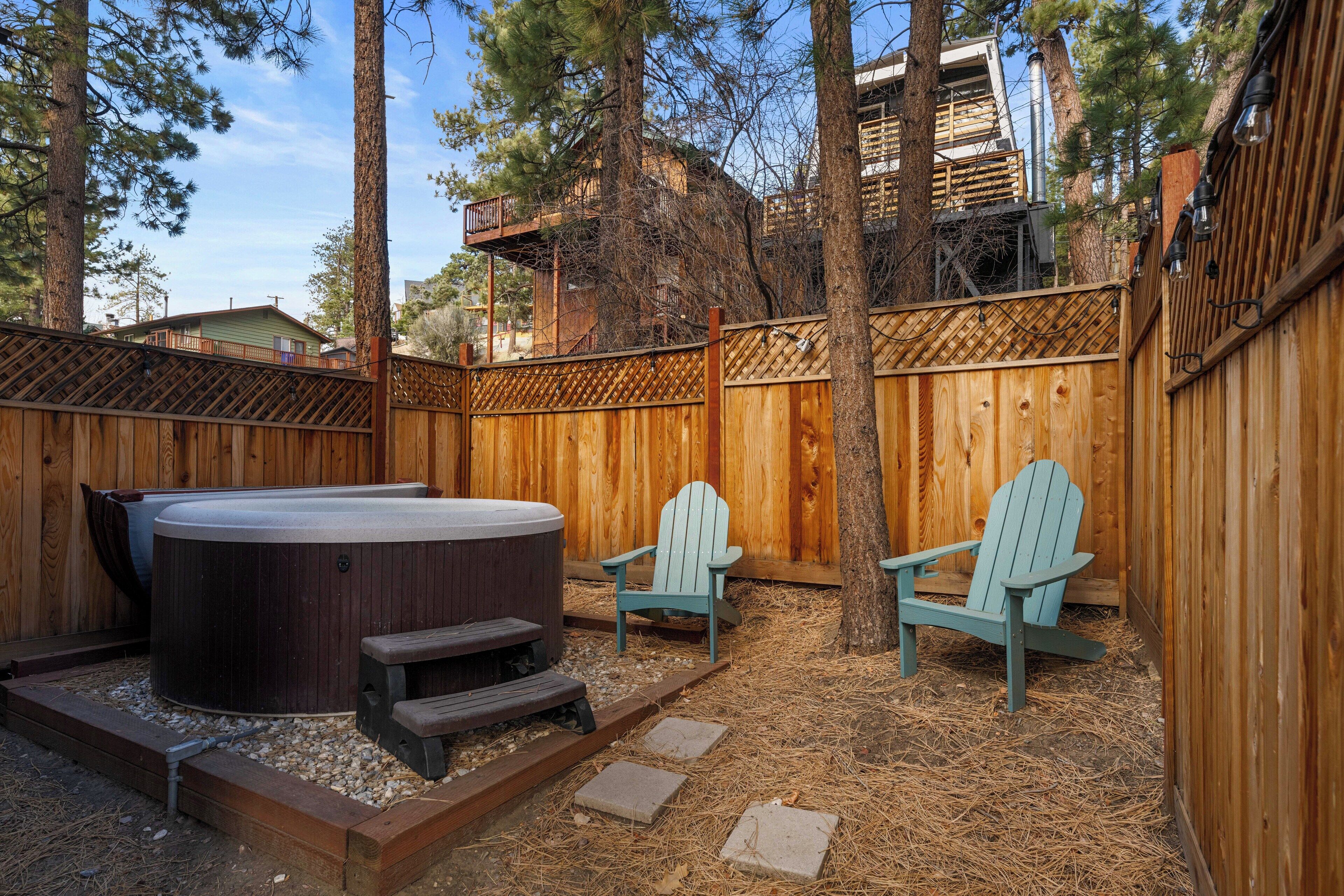 A backyard with a hot tub, two Adirondack chairs, and a wooden deck.