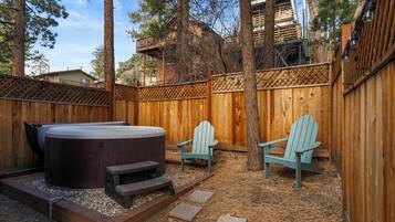 A backyard with a hot tub, two Adirondack chairs, and a wooden deck.