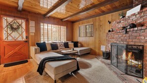 A cozy living room with a fireplace, wooden walls, and a sectional sofa. - Encino Pines (Big Bear Lake)