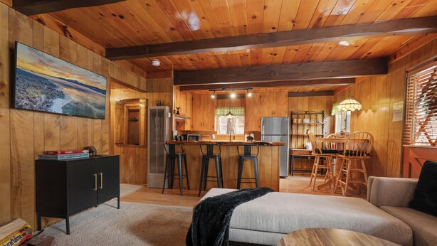 A cozy cabin interior with a living area, kitchen, and bar seating. - Encino Pines (Big Bear Lake)