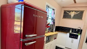 Een kleine keuken met een rode Galanz koelkast, witte kastjes, een zwart aanrecht en een zwart-wit tapijt.