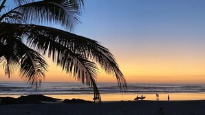 A beach scene with palm trees, ocean, and people. - SANTA TERESA SURFING VILLA N°2 PRIVATE SWIMMING POOL OCEAN VIEW (Puntarenas Province)