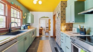A kitchen with green cabinets, a black sink, and a stove. There is a window with a wooden frame and a light fixture above the sink.