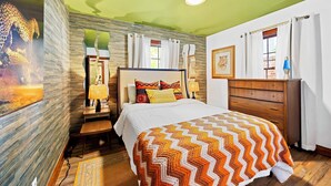 A bedroom with a bed, wooden dresser, and a nightstand with a lamp.