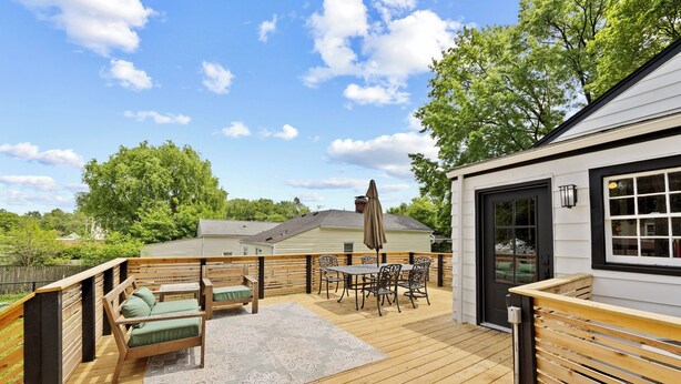 A wooden deck with outdoor furniture, a covered patio area, and a view of a house in the background.