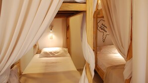 Una habitación con dos literas, cada una con una colcha y almohada blancas. Hay un aplique en la pared sobre las camas.