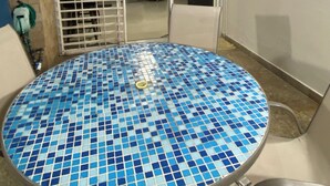 A round table with a blue mosaic tile top, surrounded by metal chairs, in a room with a sliding glass door leading to an outdoor area.