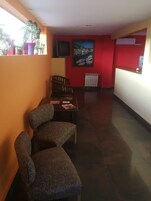 Un comedor con una mesa y dos sillas estampadas, una pared roja con un cuadro enmarcado y un piso de baldosas.