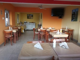 Comedor con mesas y sillas, una cocina al fondo y un ventilador de techo.