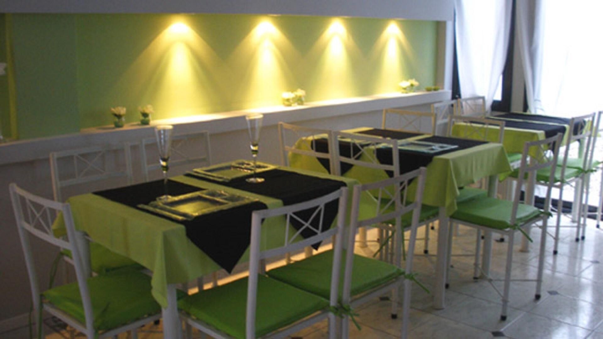 Un restaurante con mesas dispuestas para comer, sillas y una pared verde con iluminación.