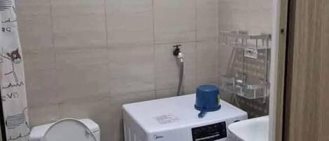 A compact bathroom with a toilet, washing machine, and sink.