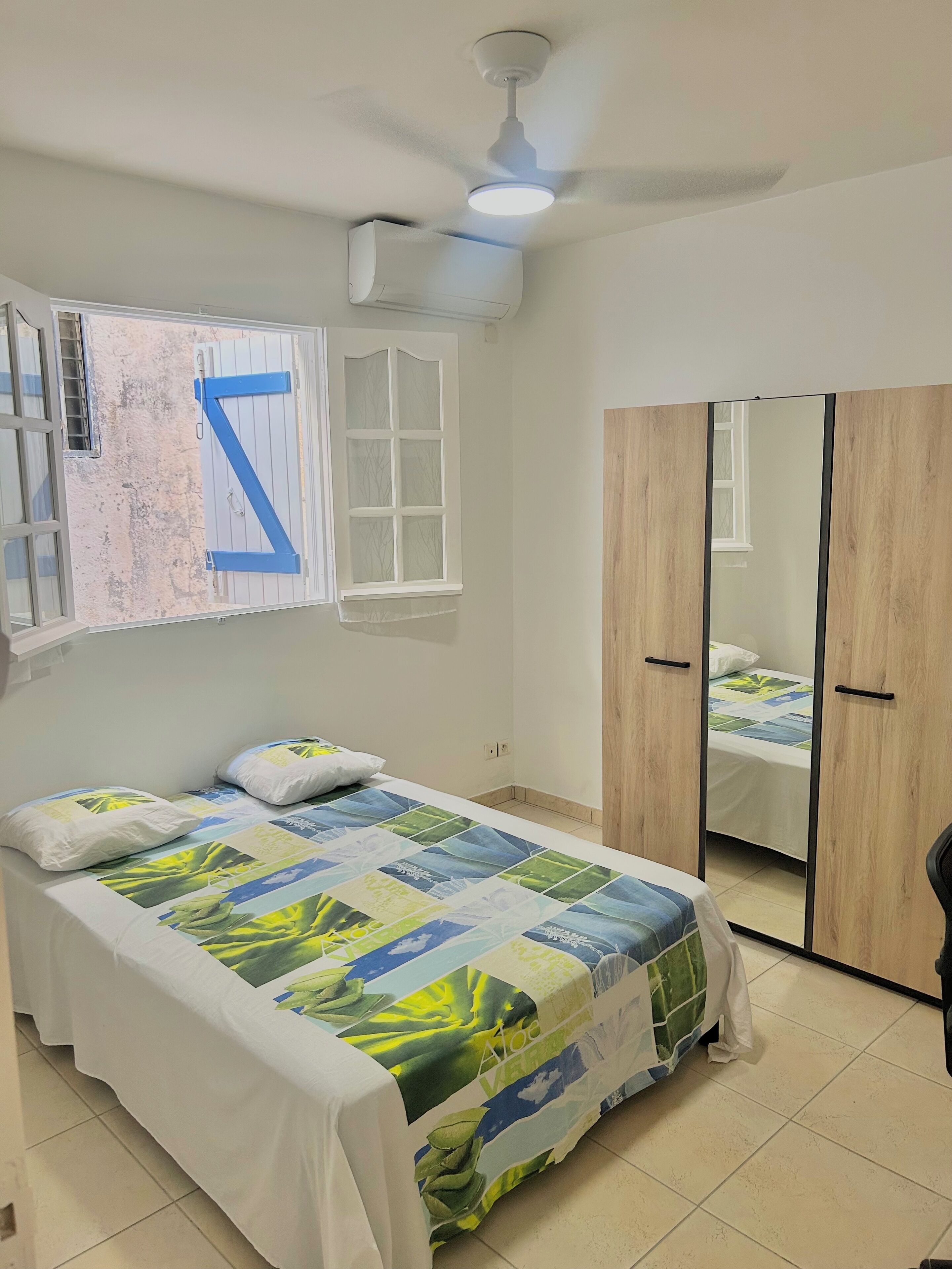 A bedroom with a bed, a wardrobe, a ceiling fan, and a window with a letter 'Z' decoration.
