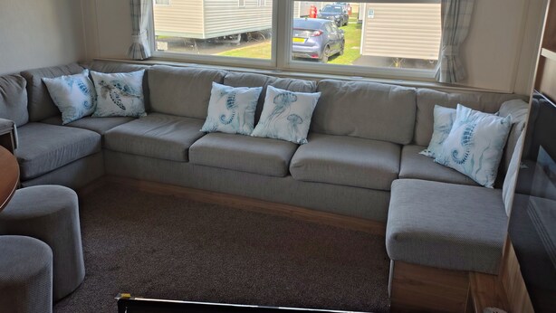 A living room with a sectional sofa, a small table, and a window with a view of a residential area.