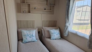 A room with two beds, each with a headboard and a pillow with a starfish design. There are wooden shelves above the beds and a window with curtains.