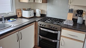 A modern kitchen with a gas stove, oven, and a toaster. There is a sink with a faucet, and wooden cabinets.