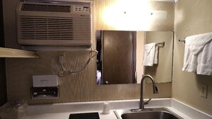 Baño de hotel pequeño con lavamanos, espejo, toallero y unidad de aire acondicionado.