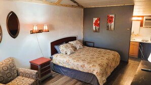 Un dormitorio con cama, mesita de noche, lámpara y una silla.