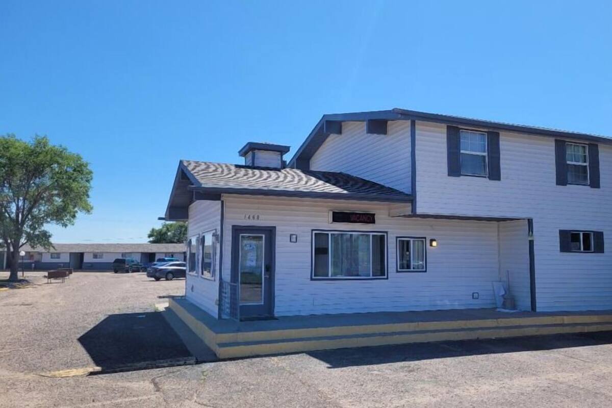 A two-story mobile home with a garage, a covered porch, and a small outdoor seating area.