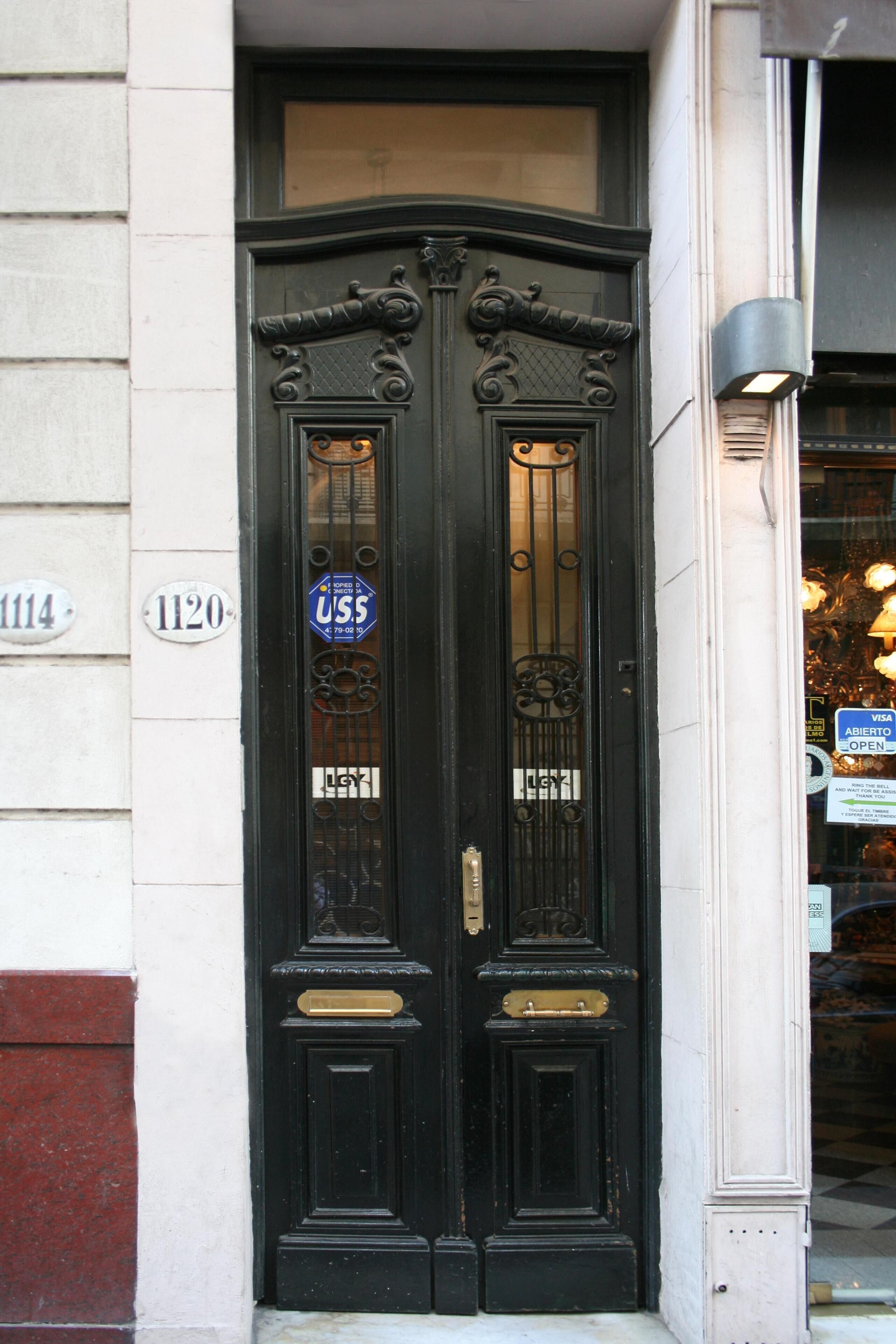 A black double door with a brass handle and a glass panel, set in a building with white and red brick walls.
