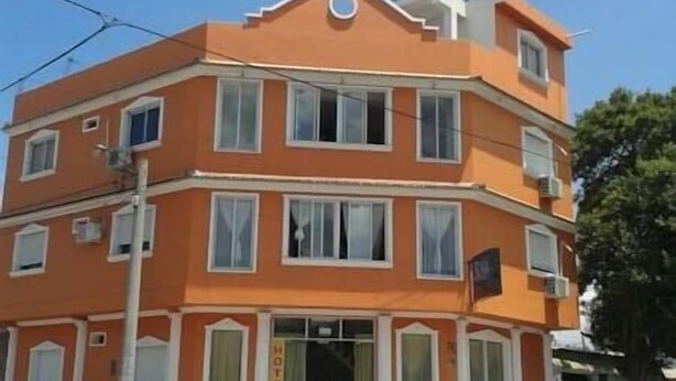 Un hôtel à plusieurs étages, doté d’une façade orange distinctive, d’une entrée centrale avec une porte noire et de nombreuses fenêtres à chaque étage.