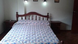 Une chambre à coucher avec un lit en bois, une couvre-lit à motifs, deux tables de chevet et des lampes fixées au mur.