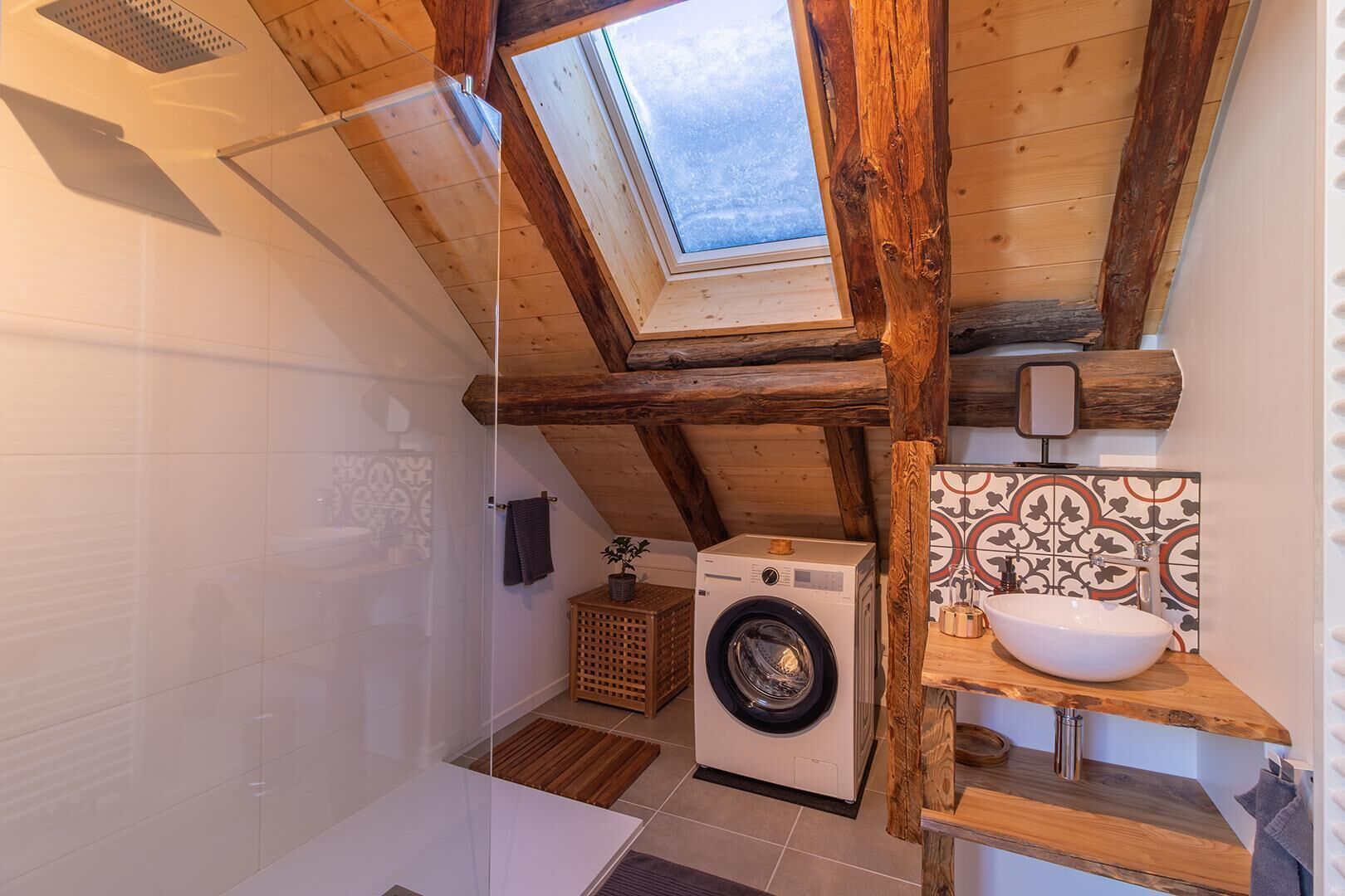 A compact bathroom with a skylight, a washing machine, and a sink with a wooden countertop.
