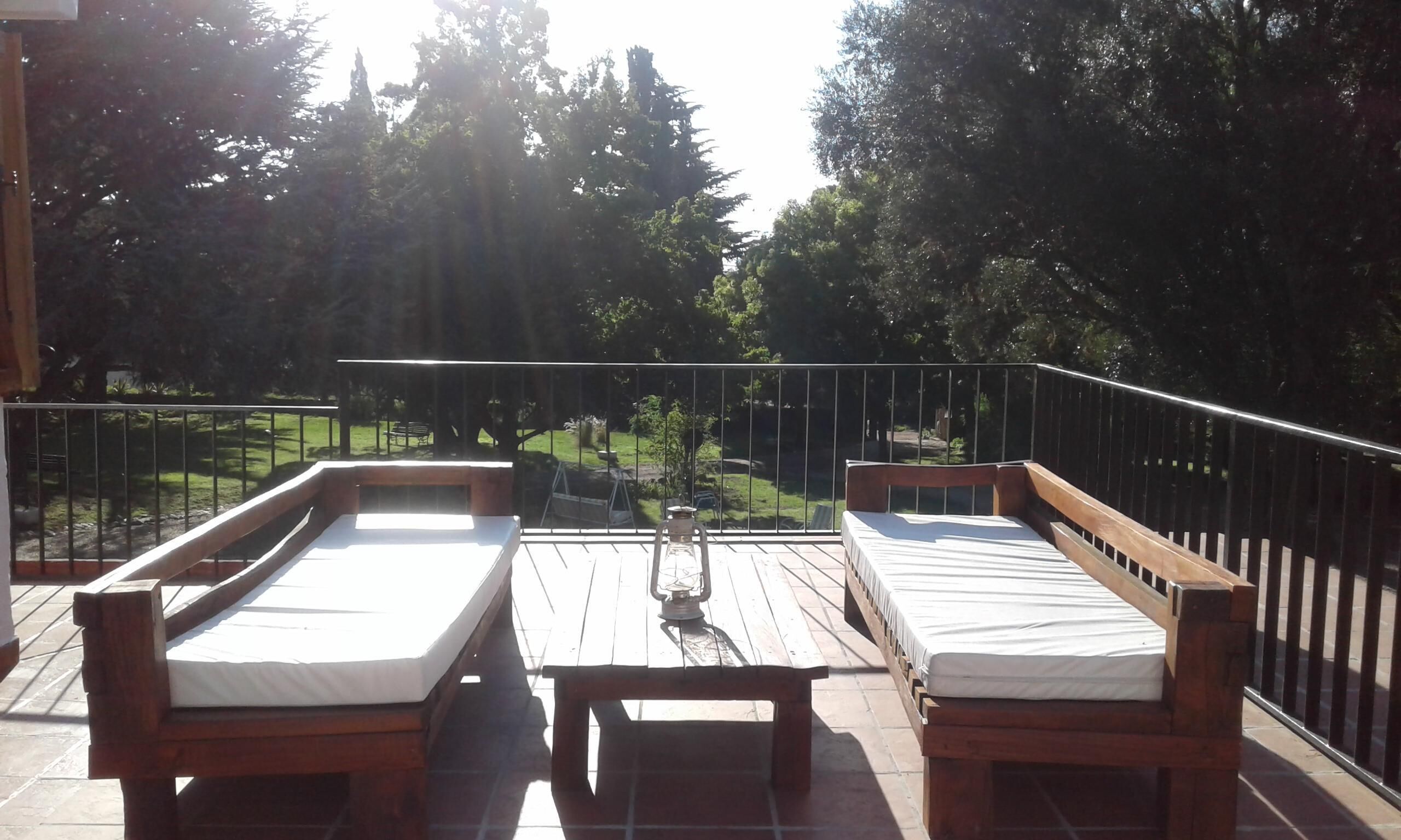 A balcony with two wooden beds and a table, surrounded by a railing.