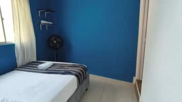 Et værelse med en seng, et vindue med gardiner, en vægmonteret ventilator og en dør.