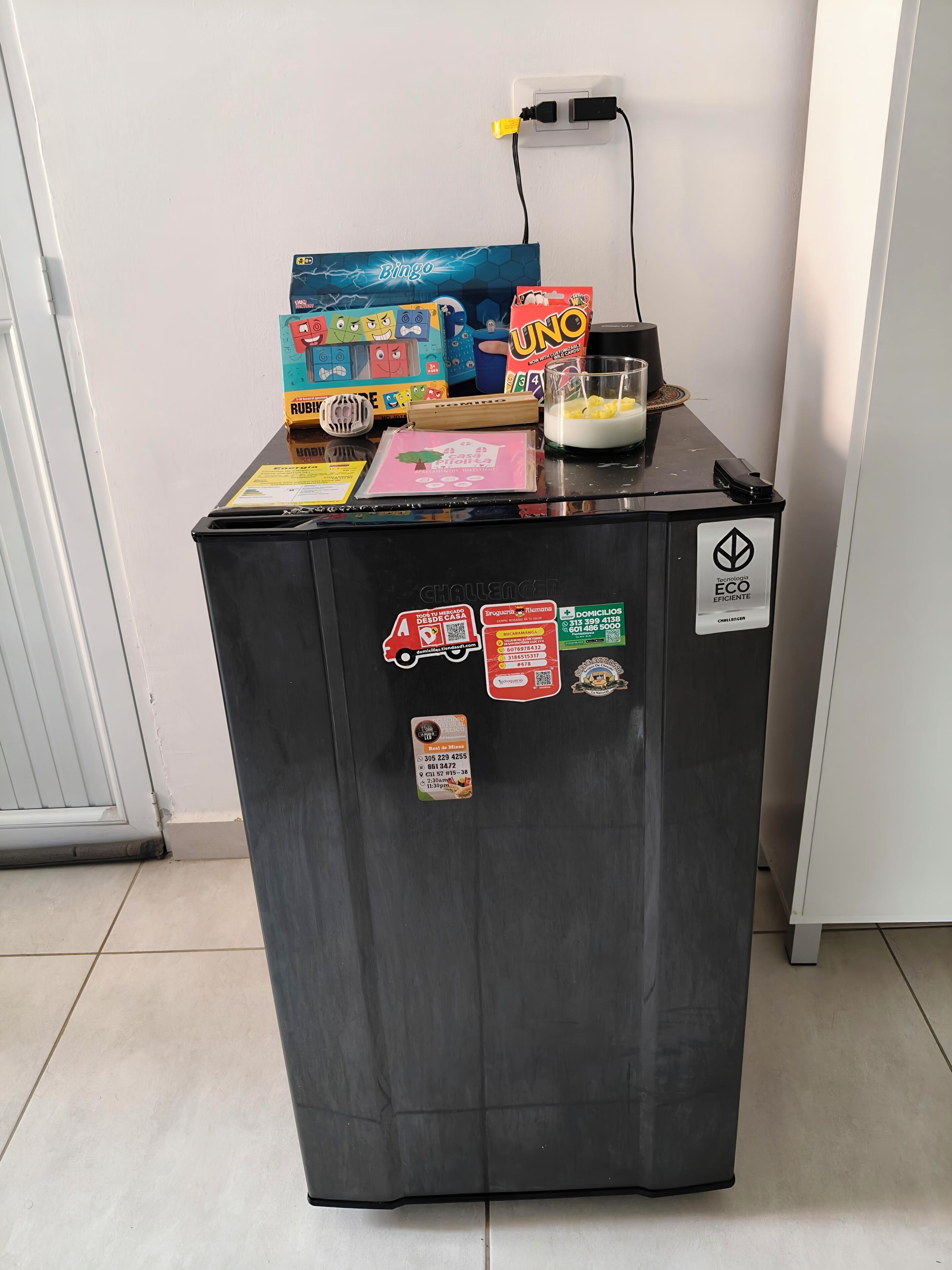Un réfrigérateur noir, sur lequel sont posés divers objets, notamment une boîte étiquetée « Bingo », un Rubik’s Cube et une boîte de jeu « UNO ».