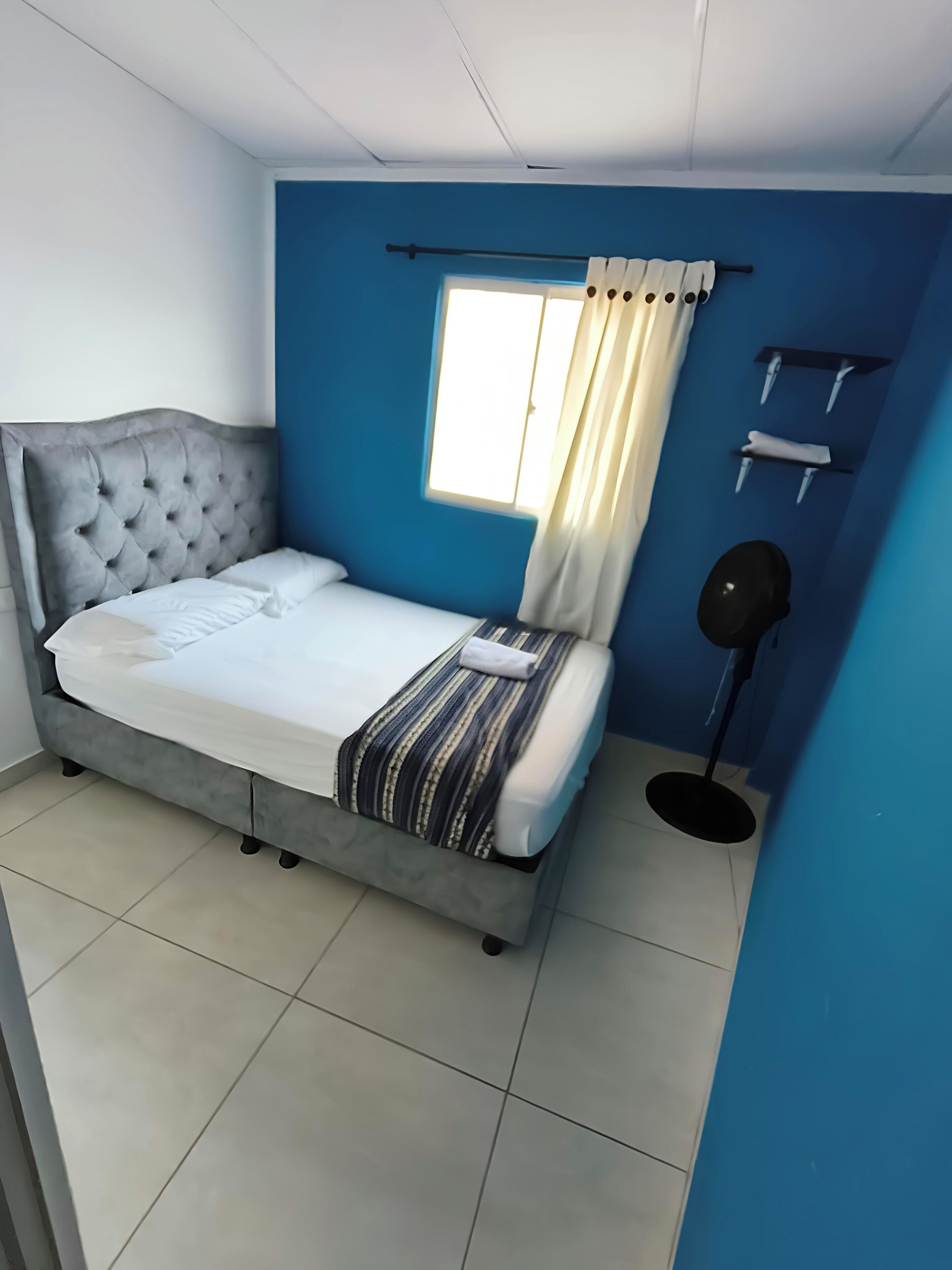 Een slaapkamer met een bed, een raam met gordijnen, een nachtkastje en een vloerlamp.