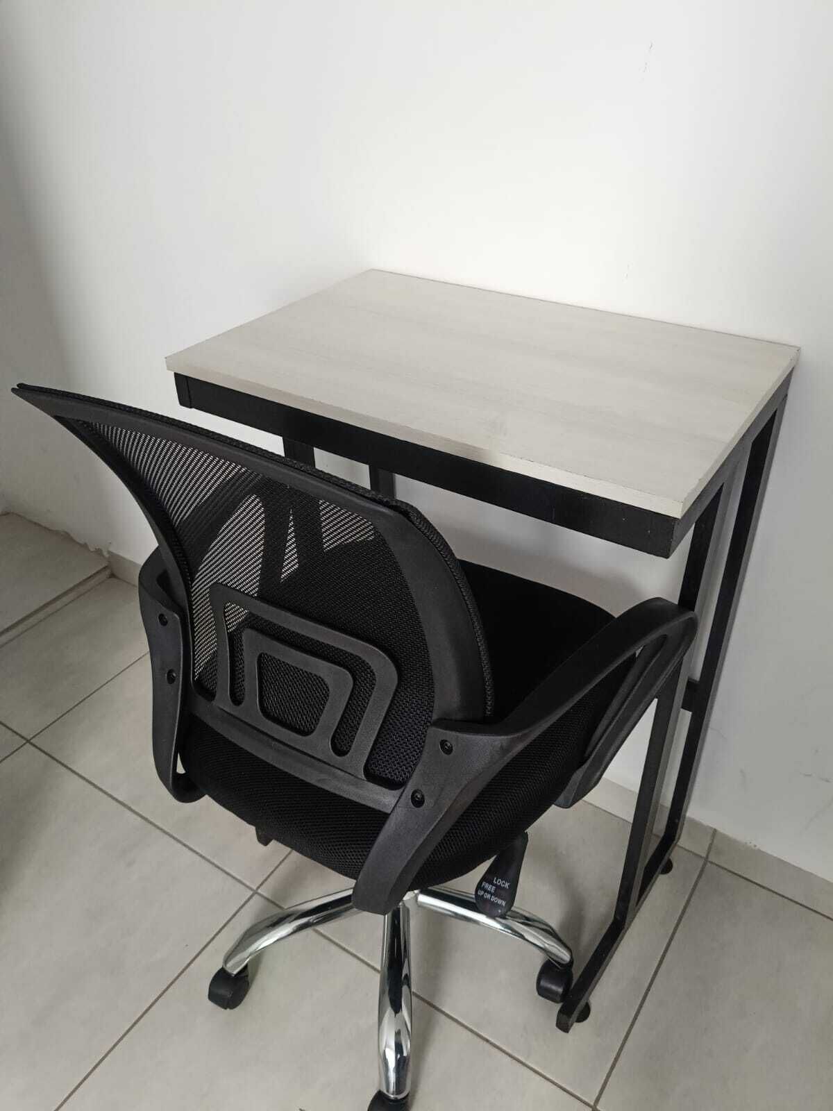Una silla de oficina negra con respaldo y reposabrazos de malla, base de metal y un escritorio de color claro con estructura negra.