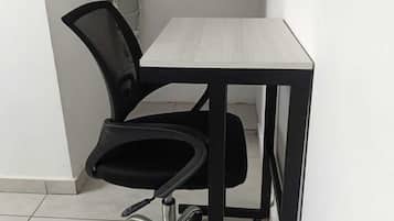 Un pequeño espacio de oficina con una silla negra, un escritorio blanco y una estantería metálica con objetos colgando.
