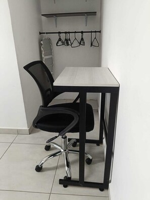 A small office space with a black office chair, a white desk, and a metal shelf with hanging items.