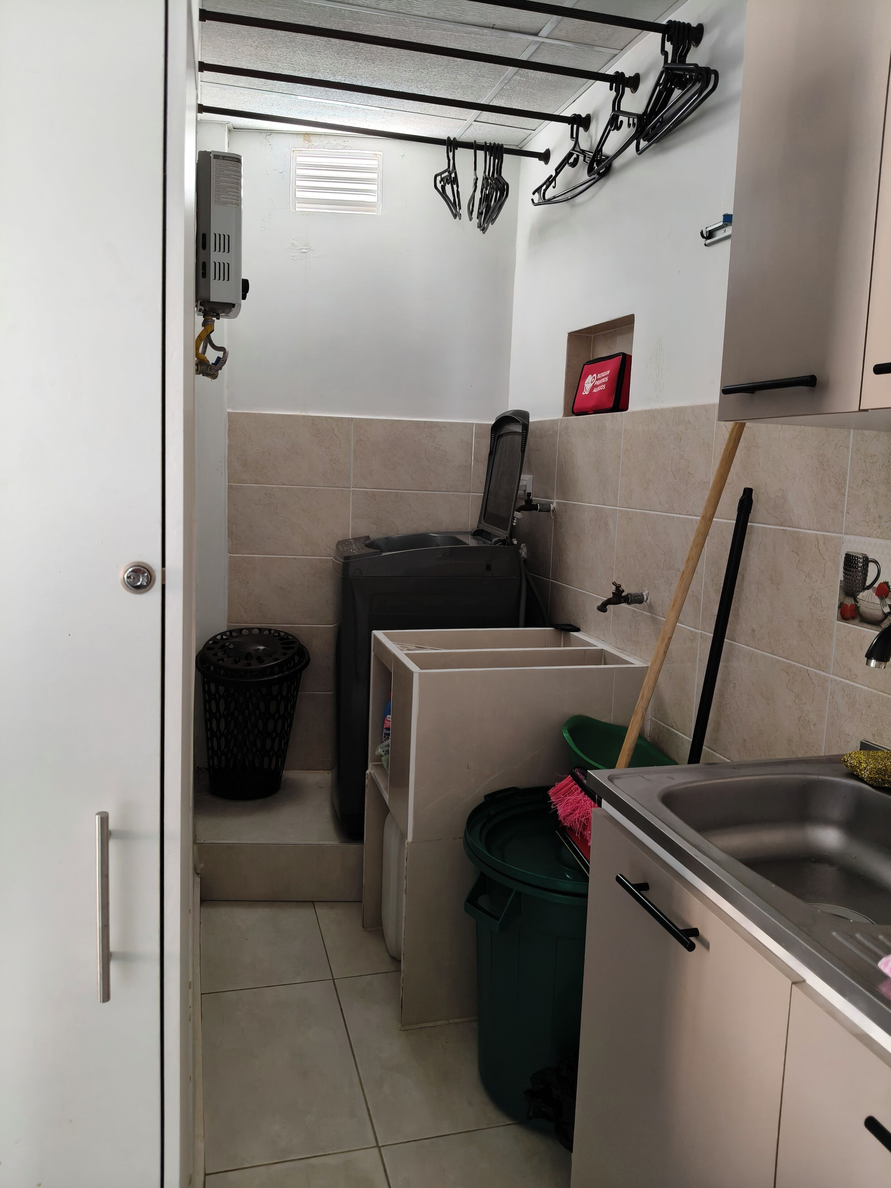 Eine kleine Küche mit Spüle, einem Mülleimer und einem an der Wand angelehnten Besen.