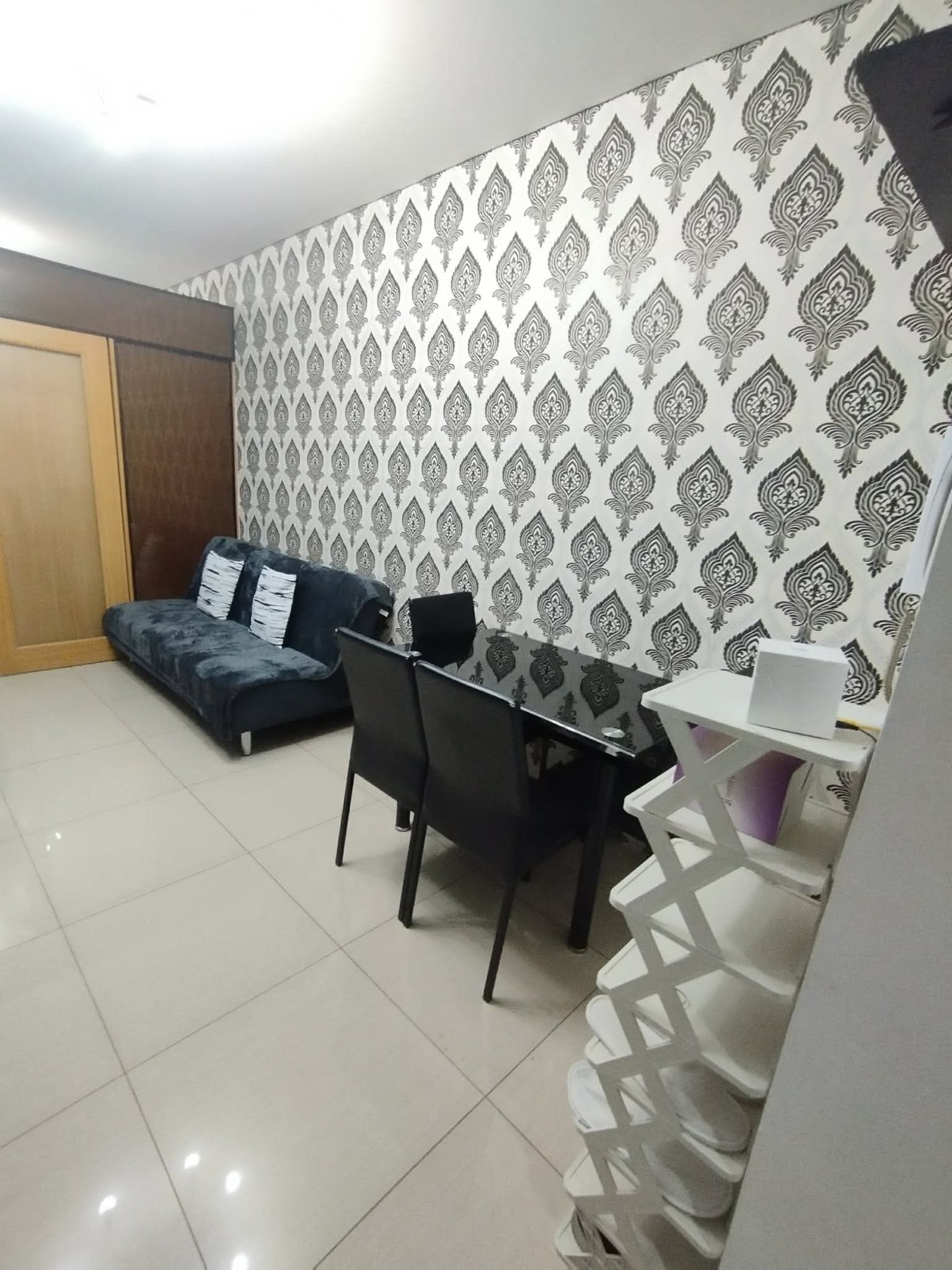 A room with a dining table, chairs, a sofa, and patterned wallpaper.
