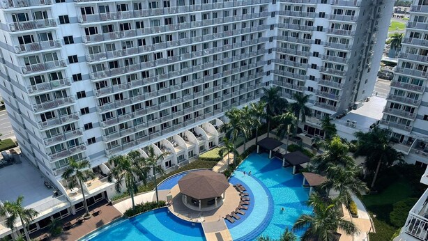 Een hoog hotel met een groot, rond zwembad, omgeven door palmbomen en loungegedeeltes.