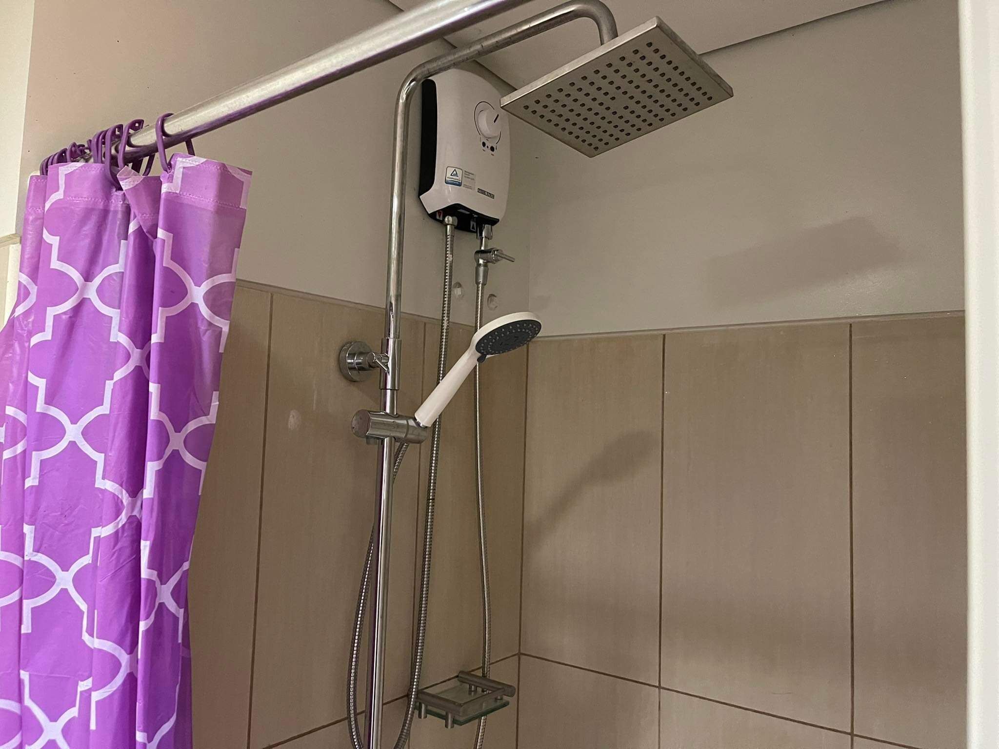 Une douche équipée d’un pommeau de douche à main et d’un pommeau de douche fixe, un rideau de douche violet orné d’un motif géométrique et un mur recouvert de carreaux.