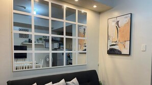 Een woonkamer met een zwarte bank, een groot raam met veel ruitjes en een schilderij aan de muur.