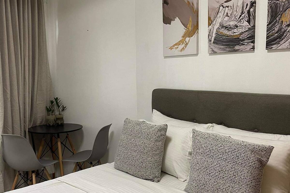 A hotel room with a bed, a small table with chairs, and three artworks on the wall.