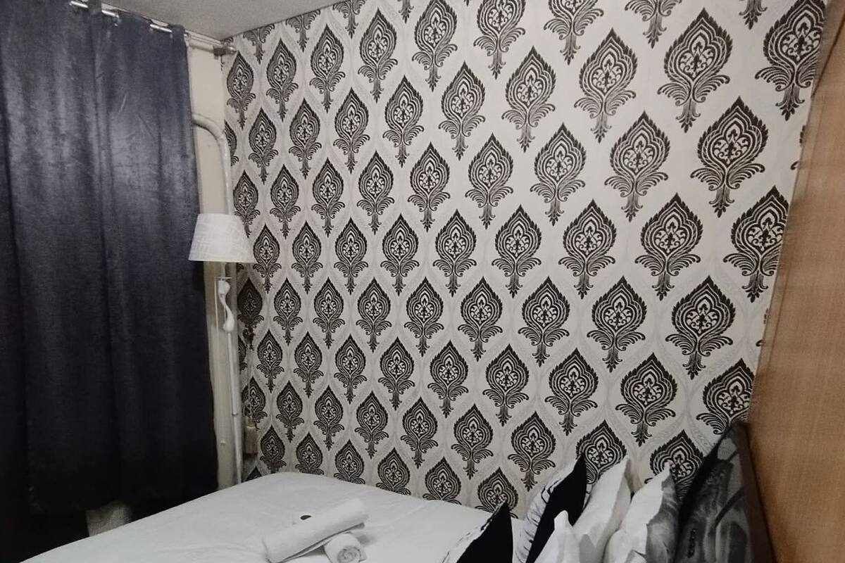 A bedroom with a bed, a patterned wall, a curtain, and a lamp.