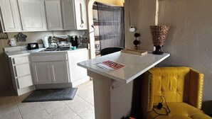 A compact kitchen with white cabinets, a small island, and a yellow armchair.