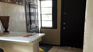 A kitchen with a tiled floor, a black door, a window, and a painting on the wall.