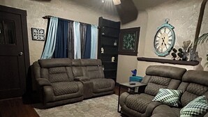 A living room with a ceiling fan, two couches, a coffee table, and a clock on the wall.